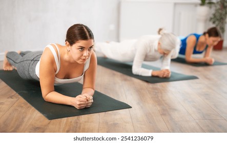 Young female yoga instructor showing others plank pose in wellness center - Powered by Shutterstock