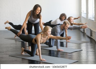 Young female yoga instructor teaching Bird dog pose, Knee to Forehead curl exercise for a group of sporty people practicing in studio, working out indoor, teacher helping to master, full length - Powered by Shutterstock