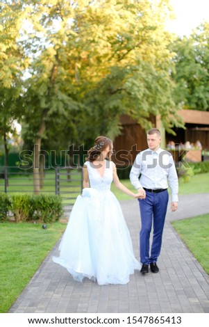 Young fiancee walking with caucasian groom in park. Concept of happy couple and wedding photo session outside.