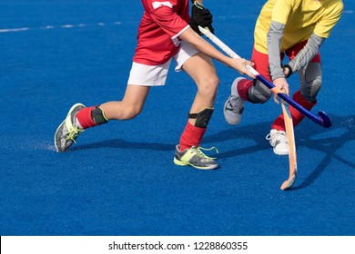 Young field hockey players on blue water based turf. Intense action between attacker in red uniform and defender in yellow, wearing gray thermal underwear - Powered by Shutterstock