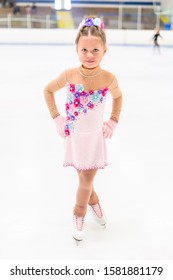 Young Figure Skater In A Pink Dress With Flowers And Rhinestones On The Indoor Ice Arena.