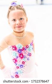 Young Figure Skater In A Pink Dress With Flowers And Rhinestones On The Indoor Ice Arena.