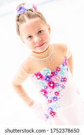 Young Figure Skater In A Pink Dress With Flowers And Rhinestones On The Indoor Ice Arena.