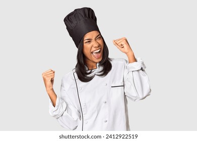 Young Filipina chef with cooking hat in studio raising fist after a victory, winner concept. - Powered by Shutterstock