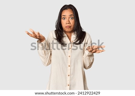 Young Filipina with long black hair in studio doubting and shrugging shoulders in questioning gesture.