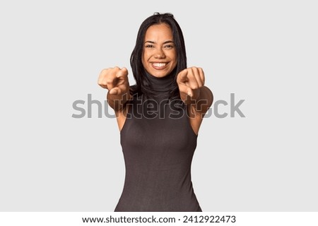 Young Filipina with long black hair in studio cheerful smiles pointing to front.