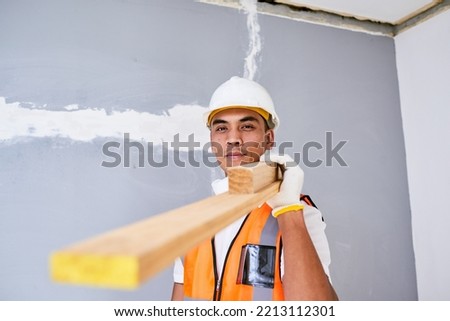 A young Filipino construction worker carries wooden planks on shoulder on site