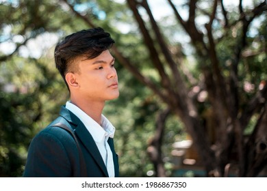 A Young Filipino Man In Deep Though, Contemplating The Future Or Problematic. Blank Stare And Emotionless, Walking Outdoors At The Park.