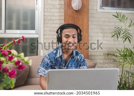 A young Filipino transcriber or chat support representative wearing noise canceling headset working at home. Example of remote job
