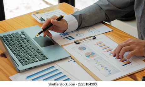 A young financial market analyst works in the office on his laptop while sitting at a wooden table. Businessman analyzing documents in hand Graph and Finance Accounting Concepts - Shutterstock ID 2223184303