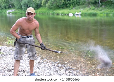 A young fireman with a naked torso. Throwing hot embers into a river with a shovel