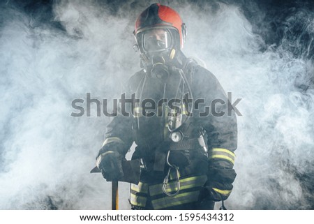 young fireman in protective coat using special equipment for fire fighting, isolated over smoky background