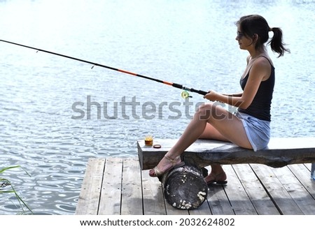 Young fisherwoman sitting on wooden pier, fishing in the lake. 