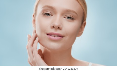 Young Fit Attractive Caucasian Blond Woman Touching Her Jaw Line And Looks At The Camera Against Blue Background | Moisturizer Advertisement