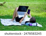 Young fit attractive hipster woman sitting on mat, green lawn in park, working browsing surfing, blogging, eshopping, using pc laptop computer. Wireless 5g internet concept. High quality photo