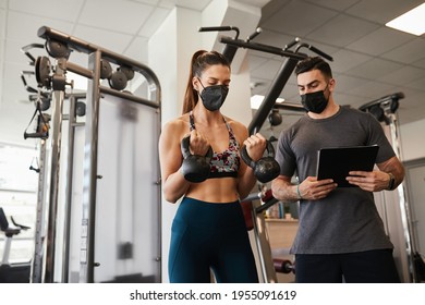 Young fit attractive woman with her personal fitness trainer doing body workout in gym. Keeping social distance and wearing protective face masks. Coronavirus pandemic sport theme. - Powered by Shutterstock