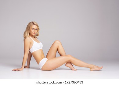 Young, fit and beautiful blond woman in white swimsuit over grey. Healthcare, diet, sport and fitness concept.