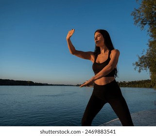 Young fit beautiful woman, practicing tai chi exercise by the river at sunset  - Powered by Shutterstock