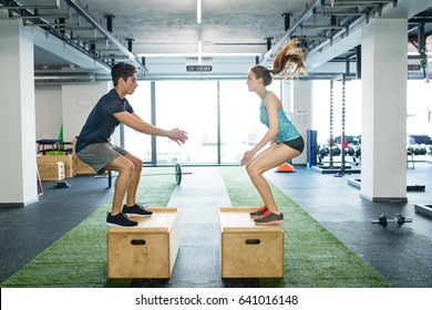 Young fit couple exercising in gym, doing box jumps.