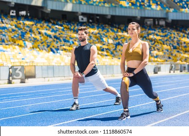 Young Fit Couple Warming Up Before Training On Running Track At Sports Stadium