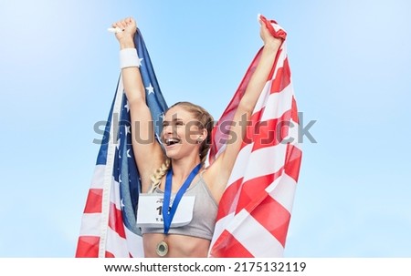 Young fit female athlete cheering and holding American flag after competing in sports. Smiling fit active sporty woman feeling motivated and celebrating achieving gold medal in olympic sport