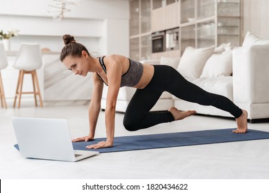 Young fit girl doing fitness exercise at home while watching online tutorial lesson on laptop. Beautiful athletic girl in leggings and top practicing yoga or workout in room. Sport, healthy lifestyle - Shutterstock ID 1820434622