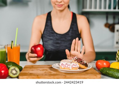 Young fit girl refuses eating doughnuts and opts for healthy food in the kitchen. Difficult choice between unhealthy sweet junk meal and vegetables fruits full of vitamins - Powered by Shutterstock