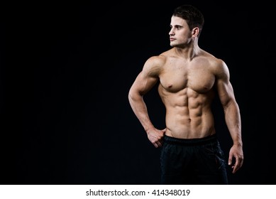 Young And Fit Male Model Posing His Muscles Looking To The Left Isolated On Black Background With Copyspace. Man Showing His Six Pack Abs On Dark Background