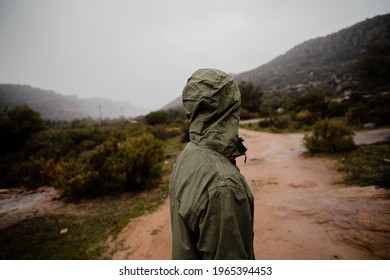 Young Fit Male Runner Resting From Running On Gravel Mountain Path In Rain With Rain Jacket Cloudy Weather Green Bushes