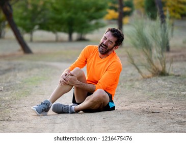 Young fit man holding knee with his hands in pain after suffering muscle injury broken bone leg pain sprain or cramp during a running workout in park outdoors in sport training running injury.