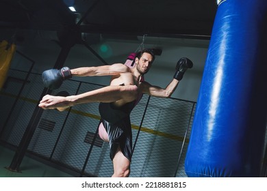 Young Fit Man Kicking A Boxing Bag At The Gym From The Side