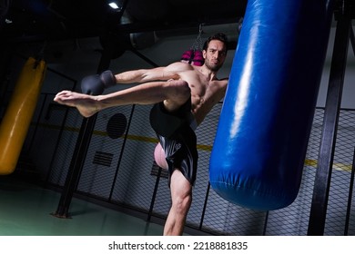 Young Fit Man Kicking A Boxing Bag At The Gym From The Side