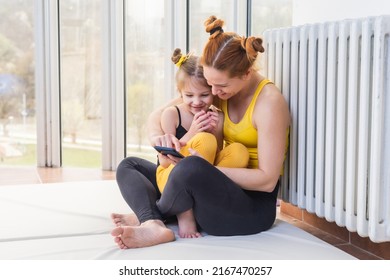 Young Fit Mom Having Loving Time With Her Daughter, Looking At A Phone Together