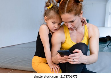 Young Fit Mom Having Loving Time With Her Daughter, Looking At A Phone Together