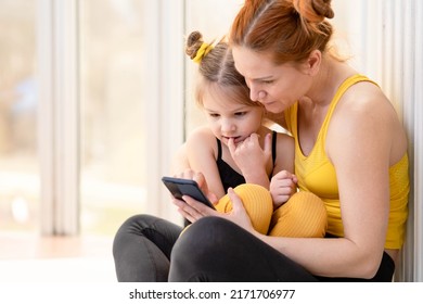 Young Fit Mom Having Loving Time With Her Daughter, Looking At A Phone Together