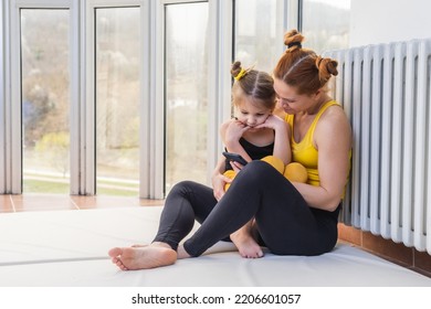 Young Fit Mom Having Loving Time With Her Daughter, Looking At A Phone Together