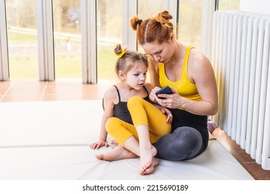 Young Fit Mom Having Loving Time With Her Daughter, Looking At A Phone Together