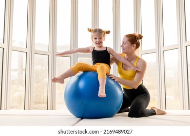 Young Fit Mom And Her Daughter Having Fun With Fitness Ball In A Gym