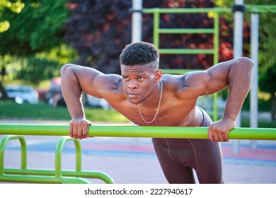 Young fit shirtless black man doing push-ups on a bar in a calisthenics park outdoors on sunny day. Fitness and sport lifestyle. - Powered by Shutterstock