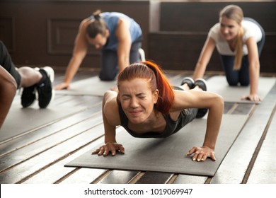 Young fit sporty woman with painful face expression doing hard difficult plank fitness exercise or push press ups feeling pain in muscles at diverse group training class in gym, endurance concept - Shutterstock ID 1019069947