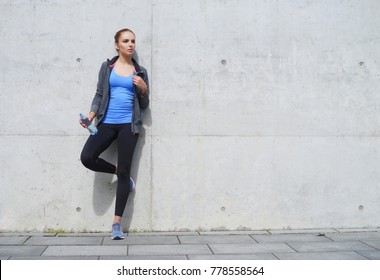 Young, fit and sporty woman standing in front of concrete cement wall. Fitness, sport, urban jogging and healthy lifestyle concept. - Powered by Shutterstock