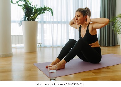 Young Fit Woman In Black Sportswear Is Doing Sit-ups At Home. Young Woman Exercising At Home Due To COVID 19 Pandemic.