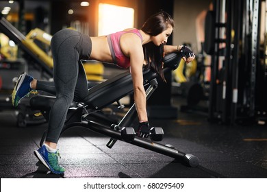Young fit woman doing back dumbbell row exercises on a bench in the gym - Shutterstock ID 680295409