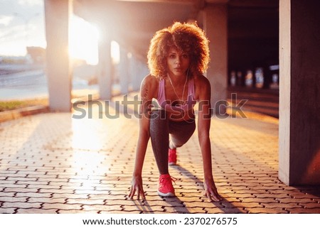 Young fit woman doing a crouch start before running under a bridge in the city