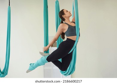 Young fit woman doing flying yoga stretch in turquoise hammock indoors. The concept of a healthy lifestyle. copy space, place for text