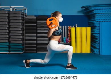 Young fit woman doing lunges at the gym wearing n95 face mask. Fitness worktout with weights under Covid-19 health crisis.