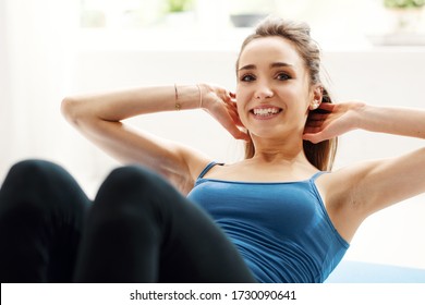 Young fit woman doing sit ups and exercising on the floor at home in the living room, fitness and sports concept