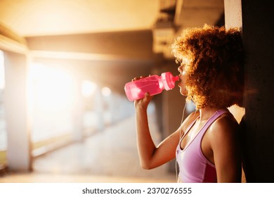 Young fit woman drinking water after jogging under a bridge in the city - Powered by Shutterstock