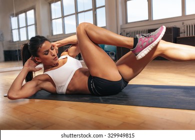 Young fit woman exercising in a gym lying on mat doing leg raising and twisting exercises. Young attractive woman doing abs workout. Fitness woman doing a sit up.