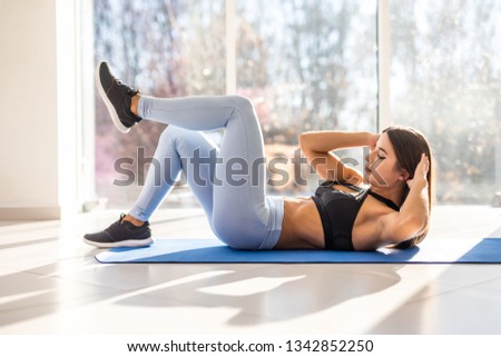 Young fit woman exercising in gym lying on mat doing leg raising and twisting exercises. Young attractive woman doing abs workout. Fitness woman doing a sit up.